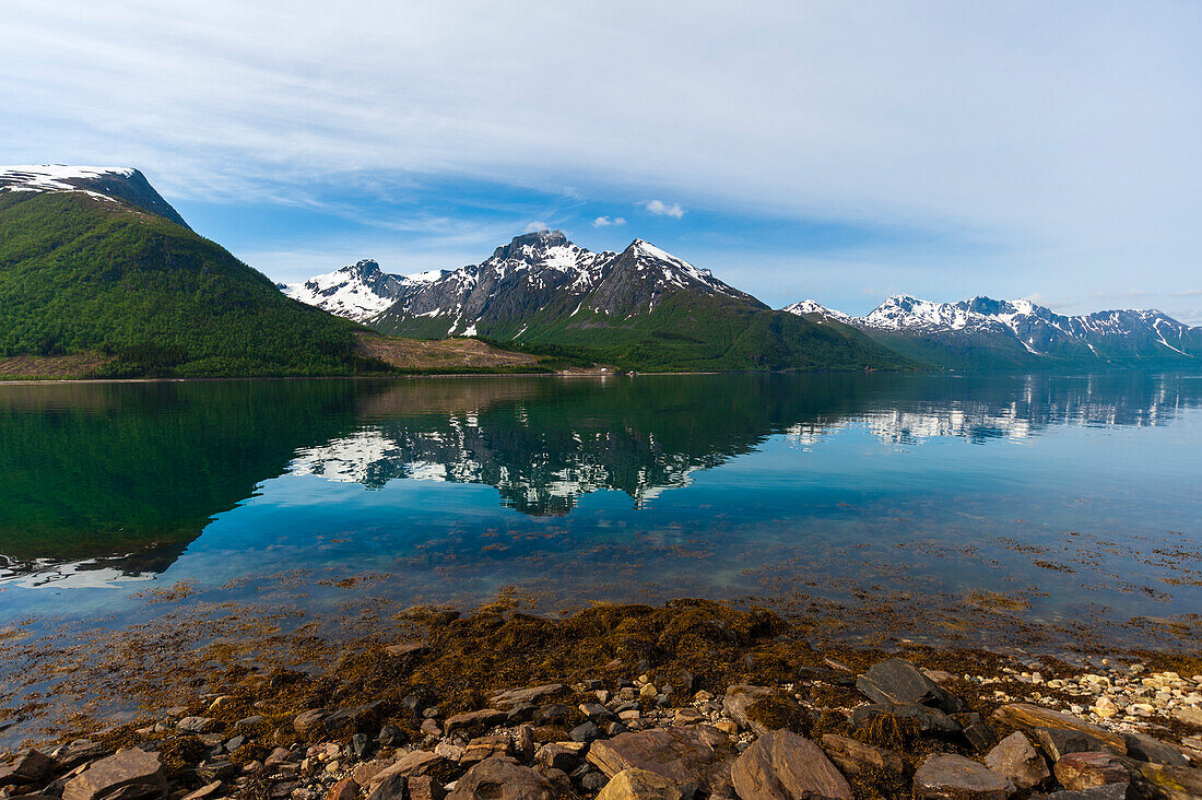 Ice streaked mountains cast a mirror reflection on Holandsfjorden's calm waters. Saltfjellet Svartisen National Park, Svartisen, Norway.