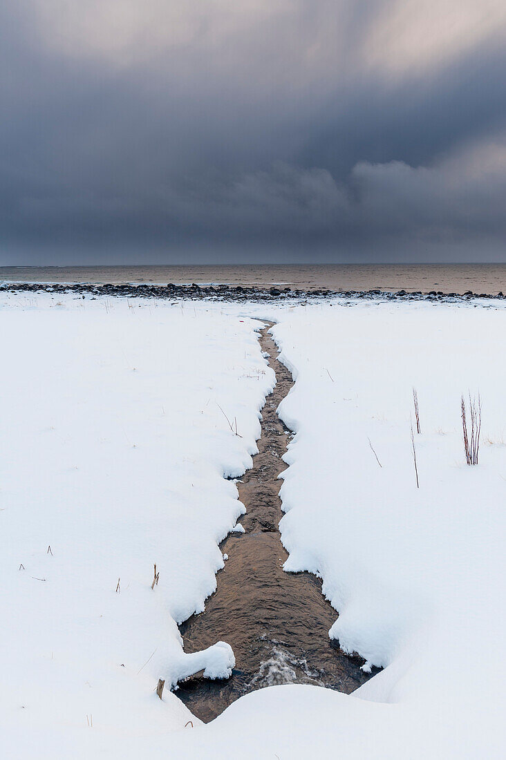 A stream leading to the sea on a snow-covered beach. Noss, Vesteralen Islands, Nordland, Norway.