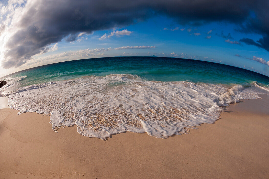 Eine Fischaugenansicht der Brandung des Indischen Ozeans, die auf einen tropischen Sandstrand trifft. Anse Macquereau Beach, Fregate Island, Republik Seychellen.