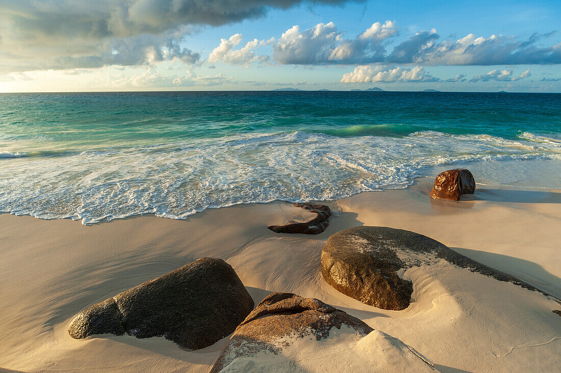 Surf surging towards boulders buried in sand on a tropical beach. Anse Victorin Beach, Fregate Island, Republic of the Seychelles.