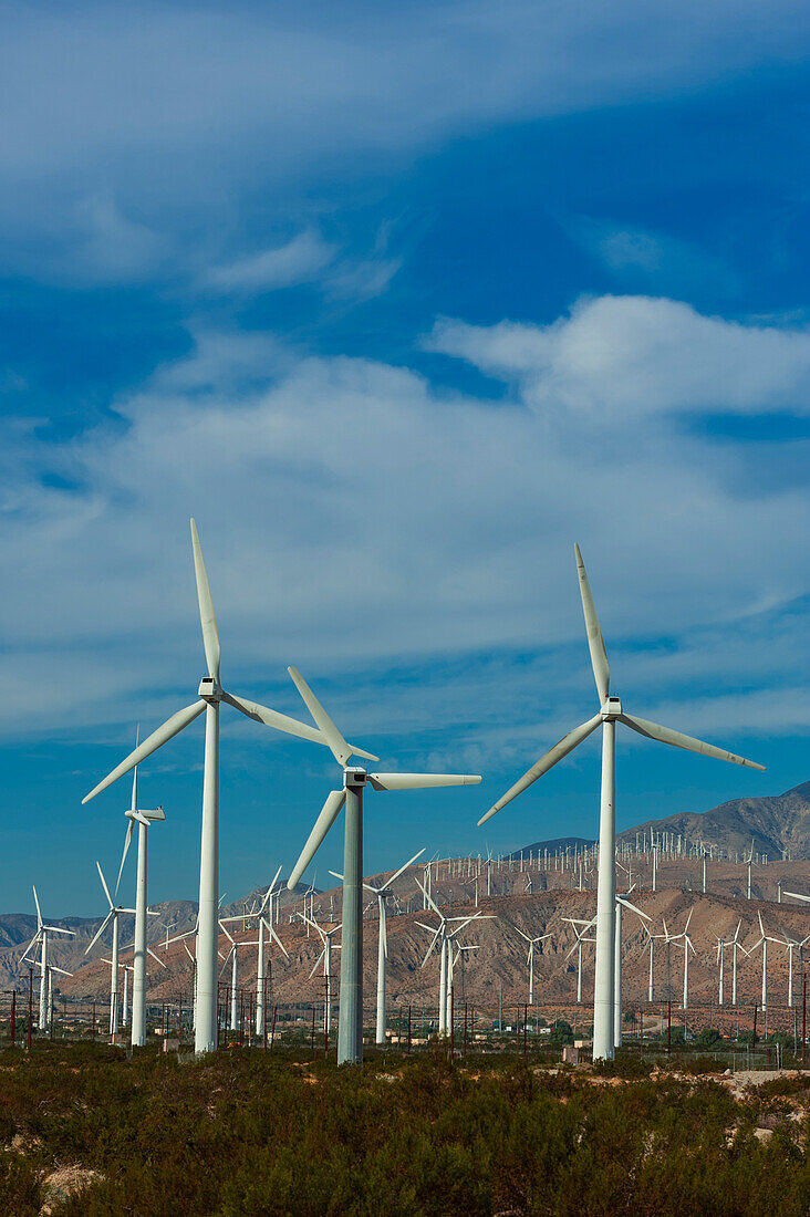 Reihen von Windrädern in einer Mittelgebirgslandschaft, mit Wolken über dem Kopf. Palm Springs, Kalifornien.