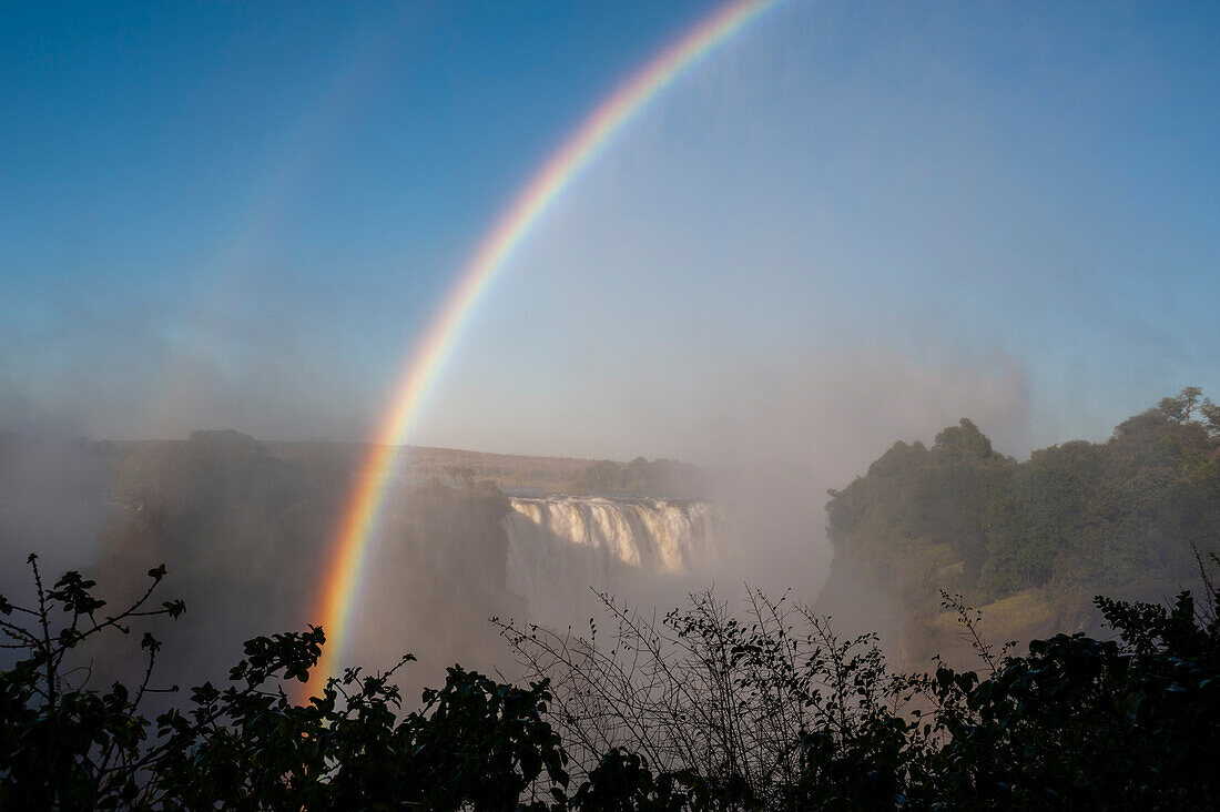 Ein doppelter Regenbogen über den nebligen Victoriafällen. Victoria Falls National Park, Simbabwe.