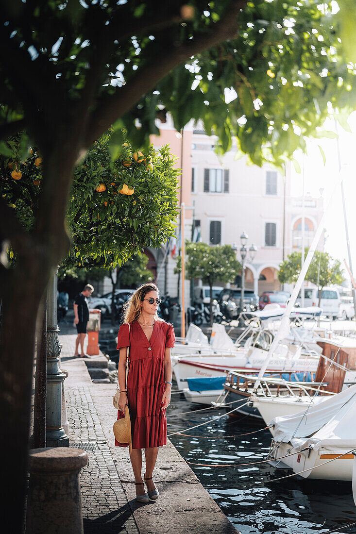 Blondes Mädchen mit rotem Kleid beim Spaziergang in Gargnano, einem kleinen Dorf am Gardasee, Provinz Brescia, Lombardei, Italien