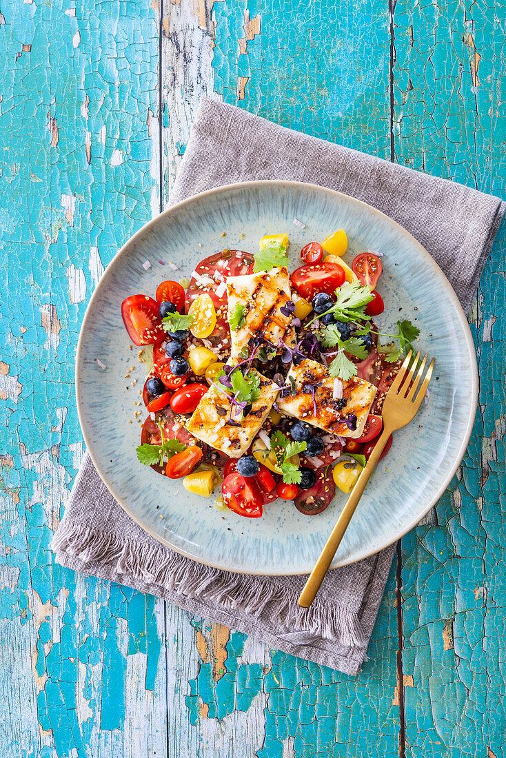 Salad with different kinds of tomatoes, grilled halloumi, blueberries and sesame dressing