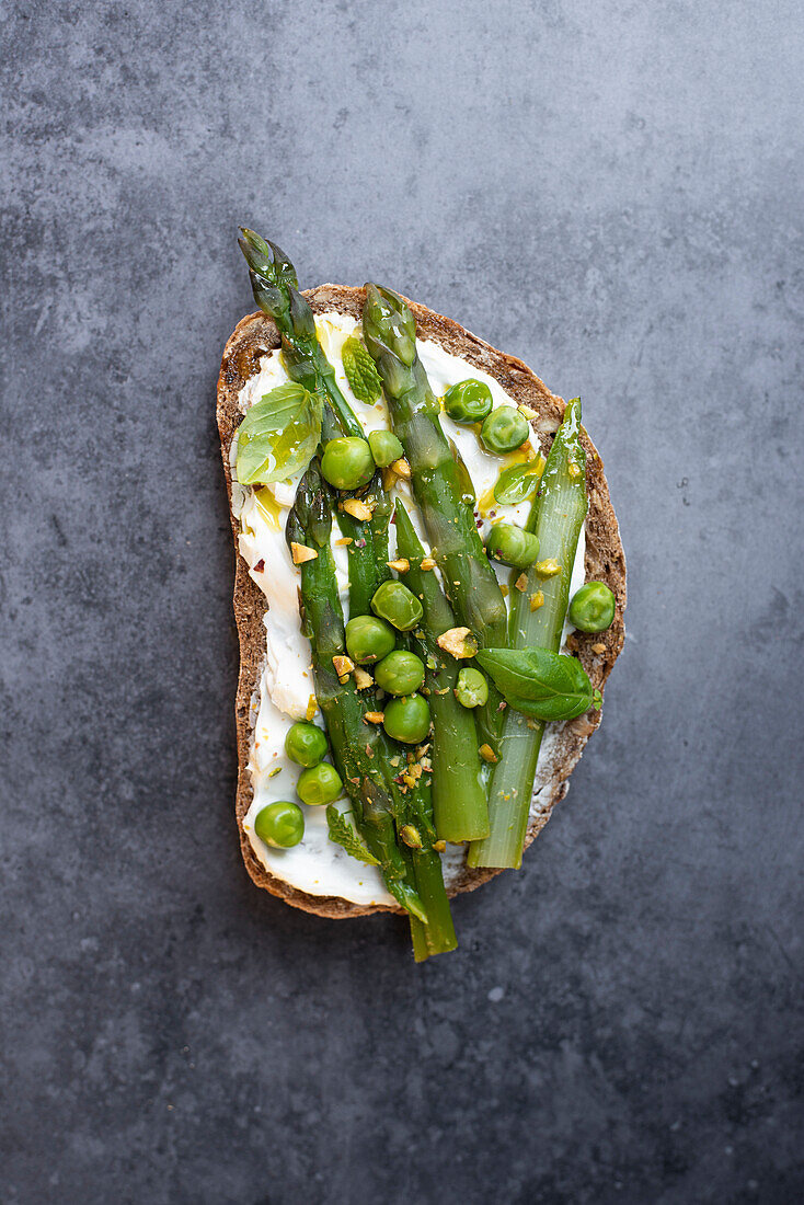 Brotscheibe mit Ziegenkäse, grünen Erbsen und Spargel