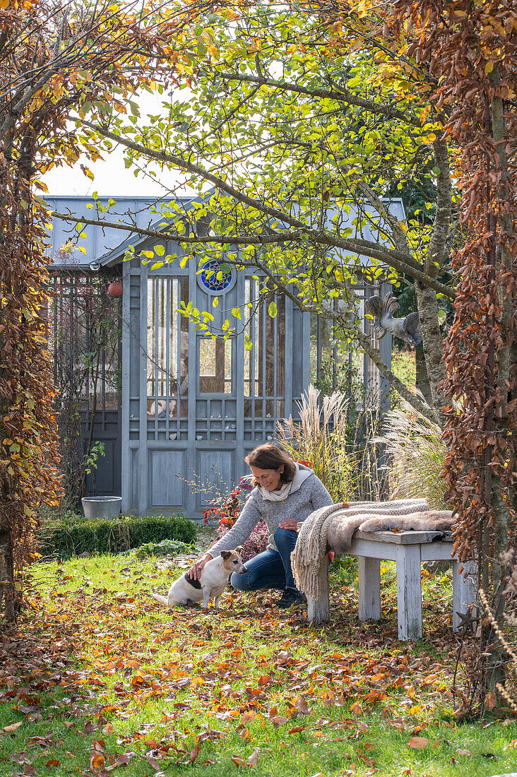 Frau mit Hund in herbstlichem Garten mit Gartenhaus, Sitzplatz