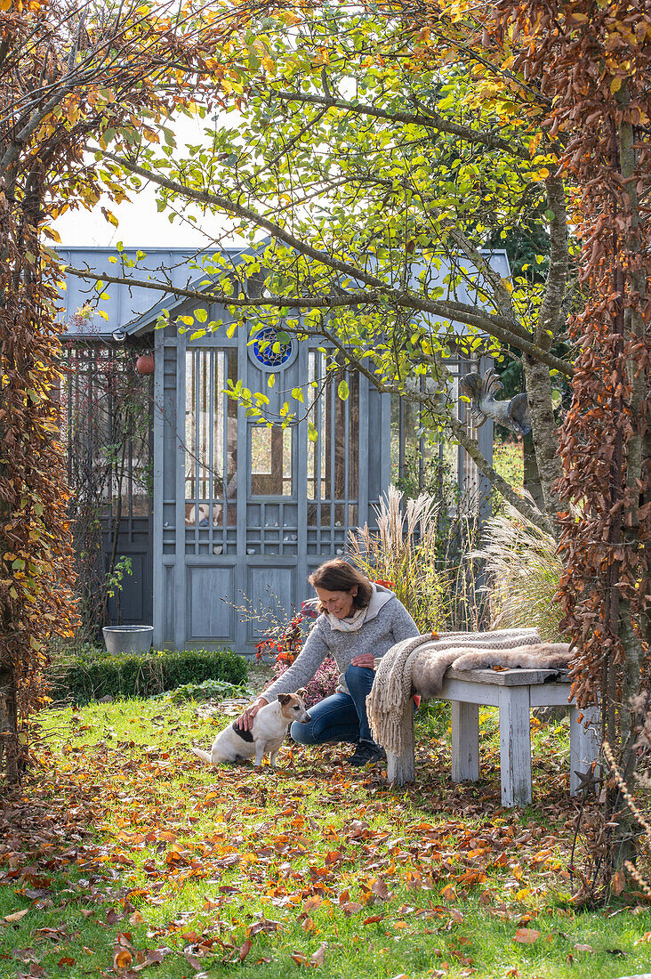 Woman with dog in autumnal garden with garden house, seat