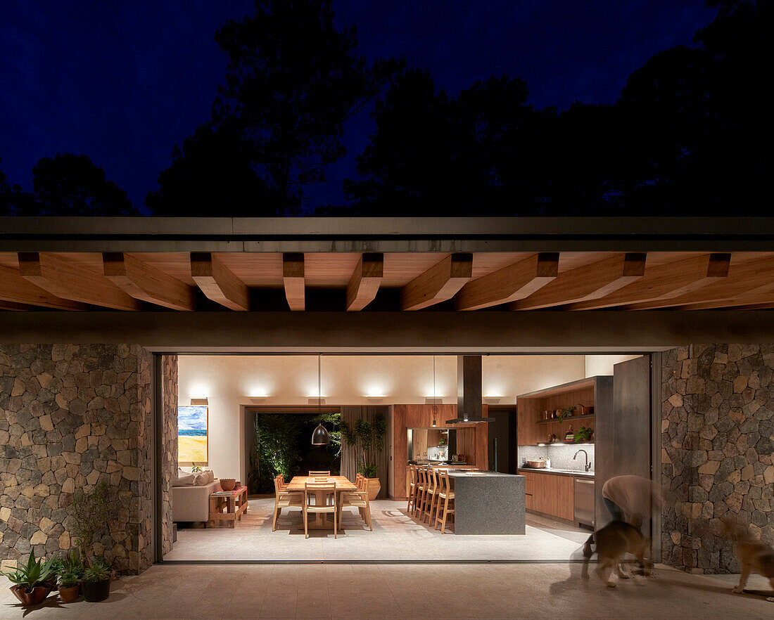 View from the terrace into open, illuminated living room in the darkness