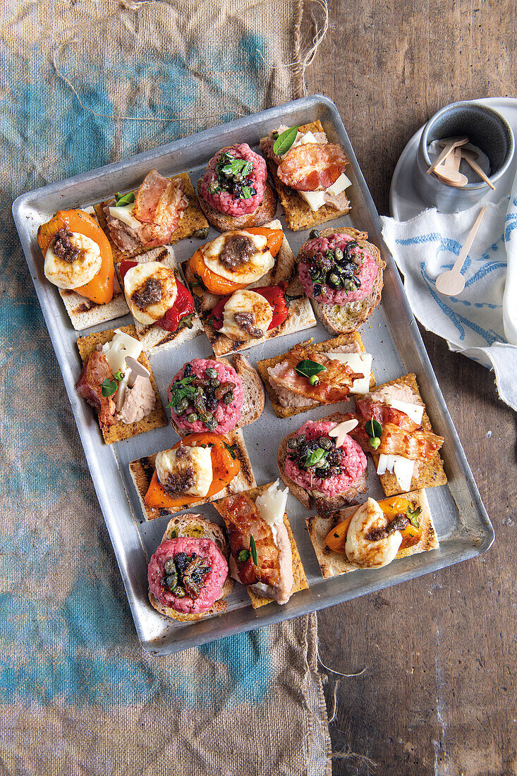 Verschiedene Häppchen mit Rindertartar, gerösteter Paprika, Scamorza-Käse und Sardellen