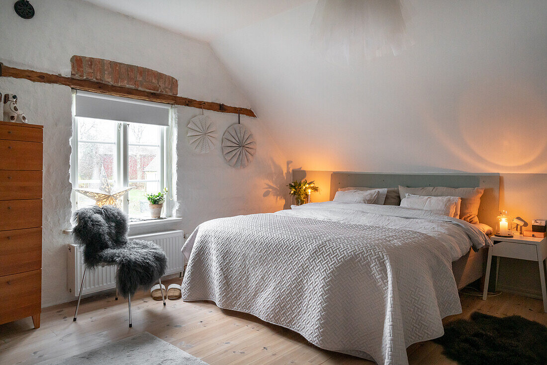 Schlafzimmer im Landhausstil mit Doppelbett und Holzkommode unter Schrägdach