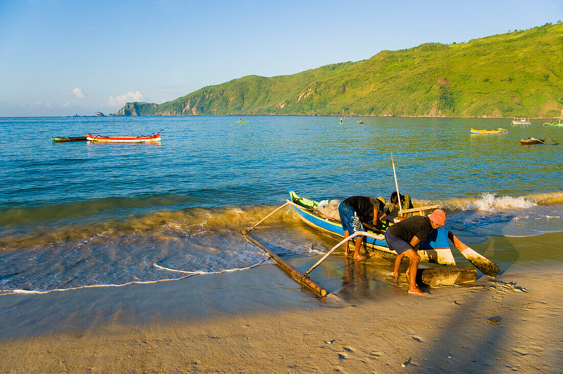 Einholen des Bootes nach der Rückkehr von einem Angelausflug am Kuta Beach, Kuta Lombok, West Nusa Tenggara, Indonesien. Das Dorf Kuta, Heimat des wunderschönen, tropischen Kuta Beach, ist ein kleines traditionelles Fischerdorf im Süden der Insel Lombok in Indonesien. Kuta Beach ist ein atemberaubender weißer Sandstrand, der von traditionellen indonesischen Fischerbooten gesäumt ist, mit denen die Einheimischen jeden Morgen und Abend zum Fischen hinausfahren.