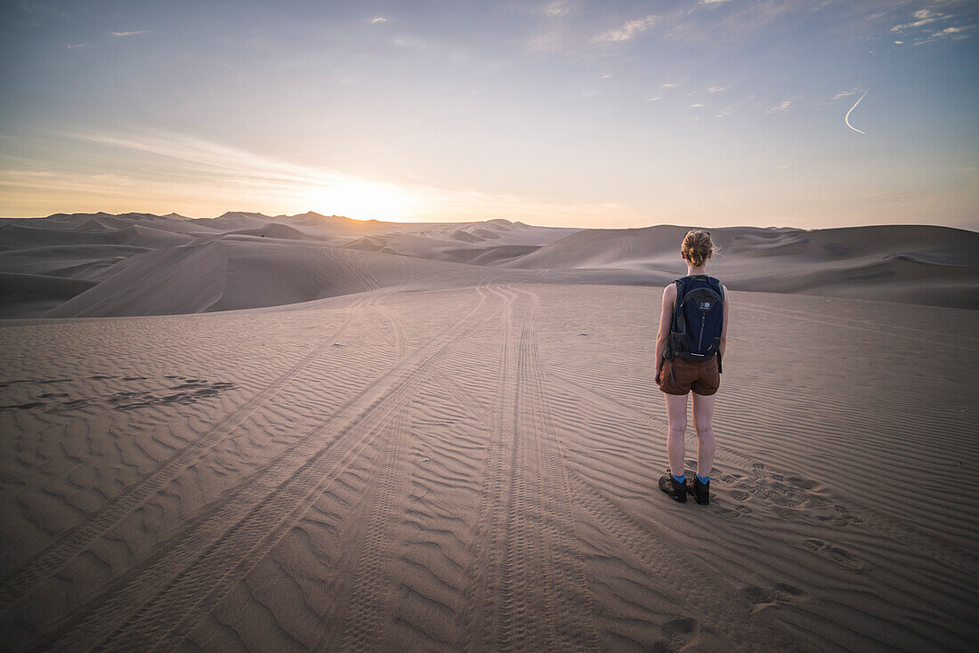 Frau betrachtet den Sonnenuntergang über Sanddünen in der Wüste von Huacachina, Region Ica, Peru