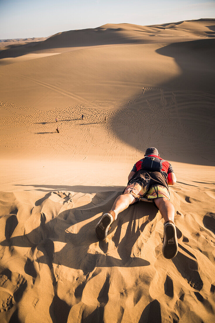 Sand boarding on dunes in the desert at Huacachina, Ica Region, Peru