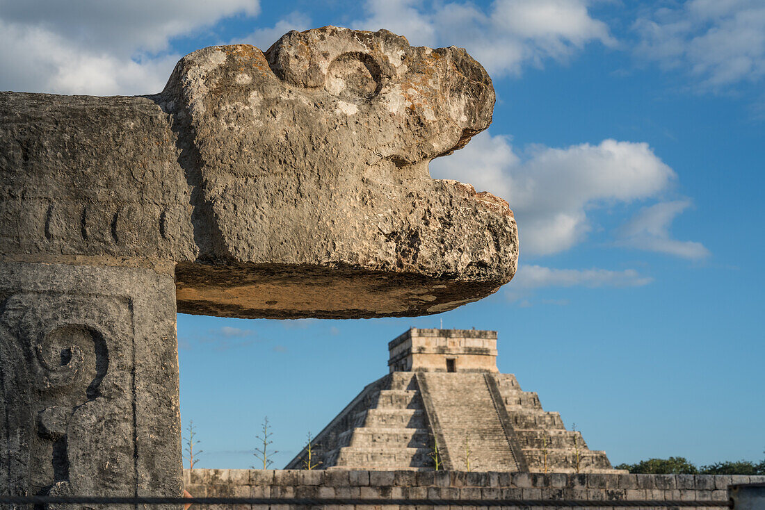Ein in Stein gehauener Jaguarkopf im Großen Ballspielplatz in den Ruinen der großen Maya-Stadt Chichen Itza, Yucatan, Mexiko. Dahinter befindet sich die große Pyramide oder der Tempel von Kukulcan, oder El Castillo. Die prähispanische Stadt Chichen-Itza gehört zum UNESCO-Weltkulturerbe.
