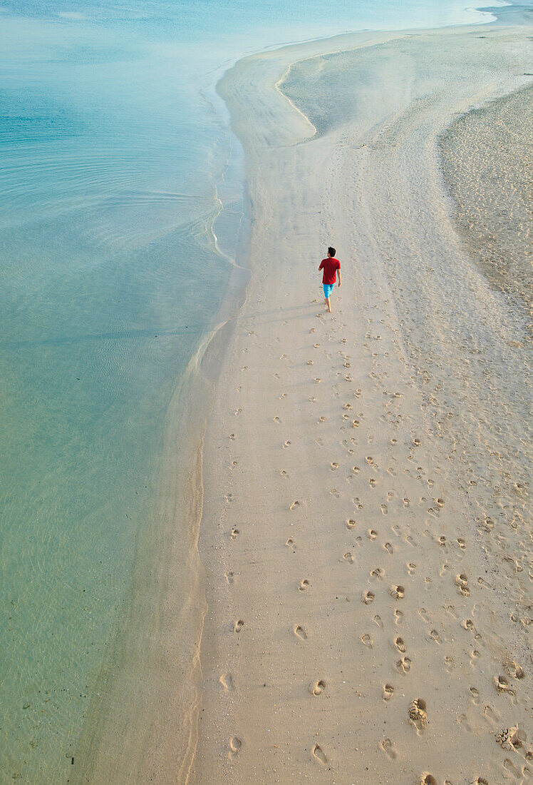 Man walking on beach next to Burj Al Arab Hotel, Dubai, United Arab Emirates.
