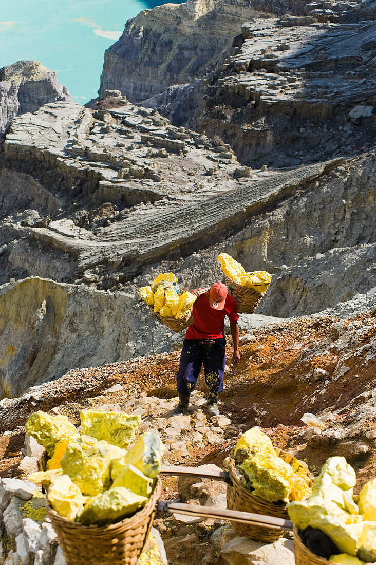 Schwefelarbeiter am Kawah Ijen, Java, Indonesien. Kawah Ijen ist ein Vulkan mit einem aktiven Krater und einem Säuresee in Ost-Java, Indonesien. Er ist ein unglaubliches und unverzichtbares Ziel für jeden, der Java oder Bali besucht. Nicht nur die Aussicht auf der 4 km langen Wanderung zum Kraterrand ist beeindruckend, sondern auch das, was sich dort abspielt, ist atemberaubend. Auf dem Weg zum Boden des Kwah Ijen (Ijen-Krater) bauen Hunderte von indonesischen Männern, viele in Flipflops, Schwefel aus dem Herzen des Vulkans ab. Sie beladen ihre Körbe mit bis zu 80 kg Schwefel, bevor sie sich a