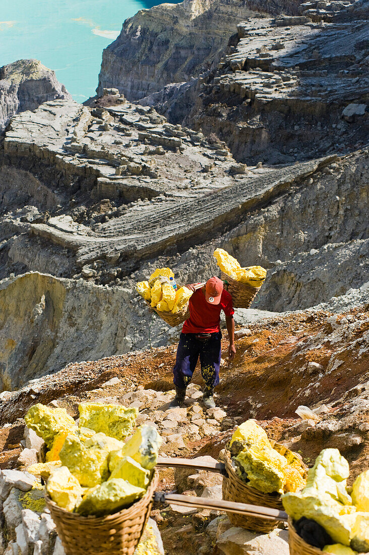 Sulphur Worker at Kawah Ijen, Java, Indonesia. Kawah Ijen is a volcano with an active crater and acid lake in East Java, Indonesia. It is an unbelievable and unmissable destination for anyone visiting Java or Bali. Not only is the view on the 4km walk up to the craters edge impressive, but what goes on there is mind boggling. Walking down to the bottom of Kwah Ijen (Ijen Crater), hundreds of Indonesian men, many in flipflops, are mining sulphur from the heart of the volcano. They load their baskets up with up to 80kg of sulphur, before starting the arduous and extremely dangerous scramble up 3
