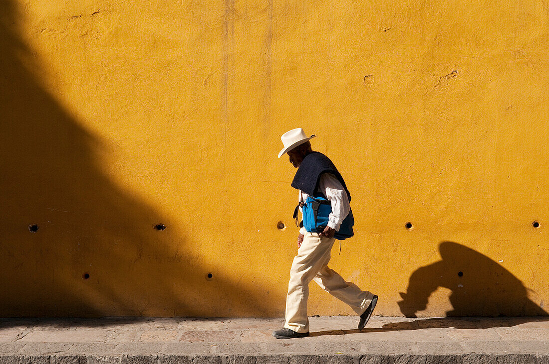 Mann, der vor einer gelben Wand spazieren geht; San Miguel de Allende, Guanajuato, Mexiko.