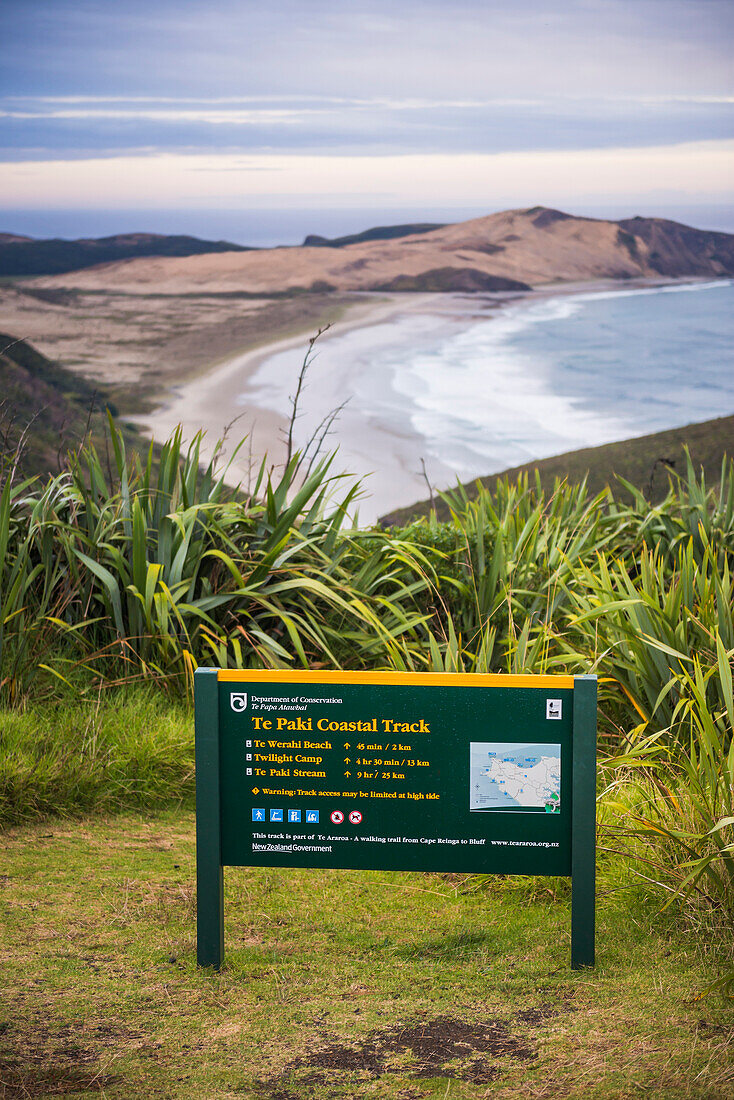 Schild des Te Paki Coastal Track, dahinter der Te Werahi Beach, Cape Reinga, Neuseeland