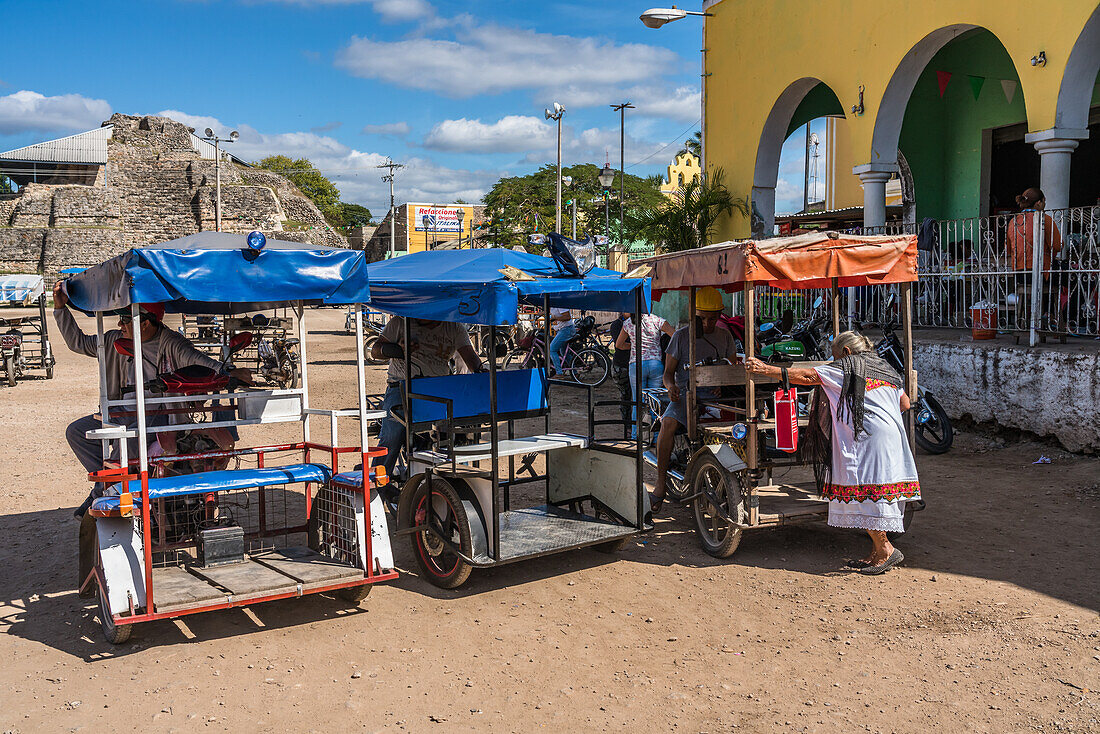 An indigenous Mayan woman in a traditional embroidered huipil gets in a motorcycle taxi in front of the market in Acanceh, Yucatan, Mexico.