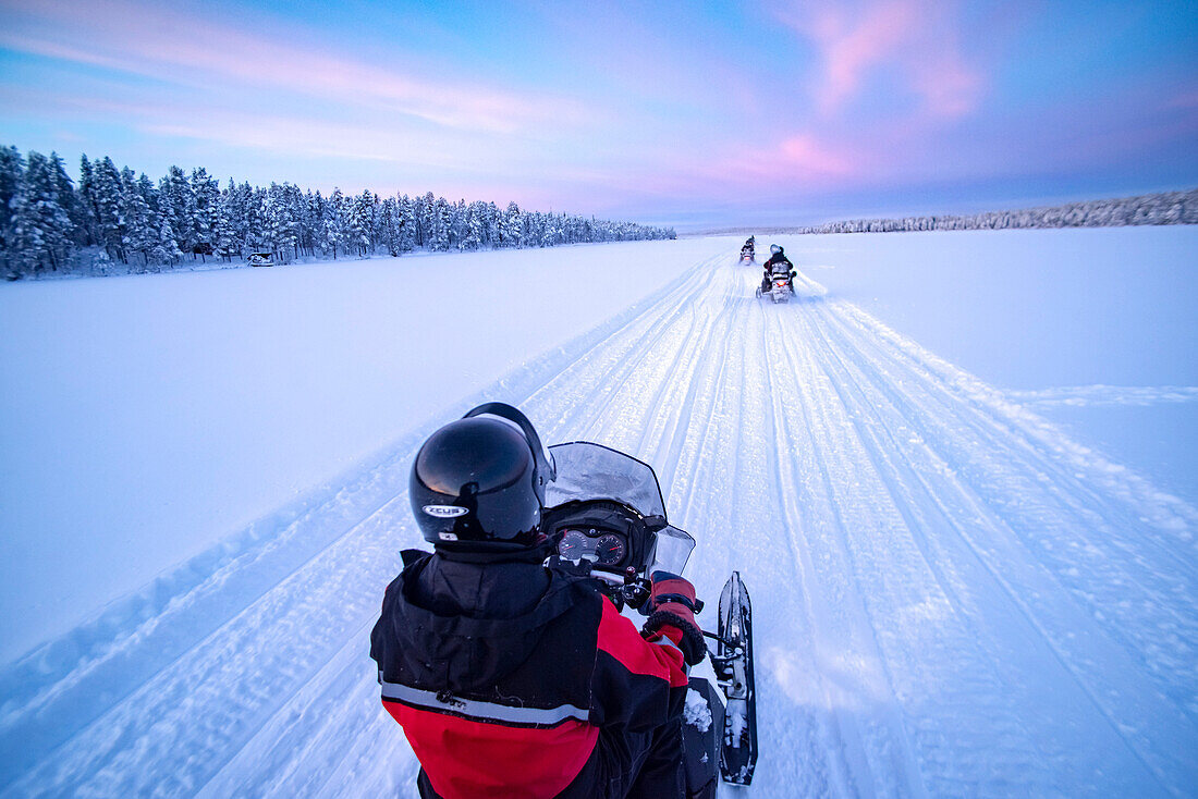 Snowmobiling on the frozen lake at sunset at Torassieppi, Lapland, Finland