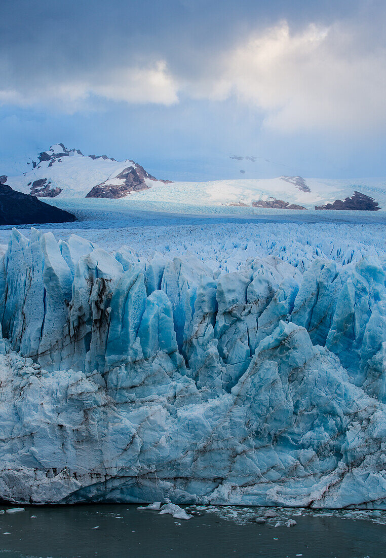 Die zerklüftete Wand des Perito-Moreno-Gletschers und der Lago Argentino im Los-Glaciares-Nationalpark in der Nähe von El Calafate, Argentinien. Ein UNESCO-Weltnaturerbe in der Region Patagonien in Südamerika. Eisberge, die vom kalbenden Eis des Gletschers stammen, schwimmen im See. In der Ferne ist der Cerro Gardener zu sehen.