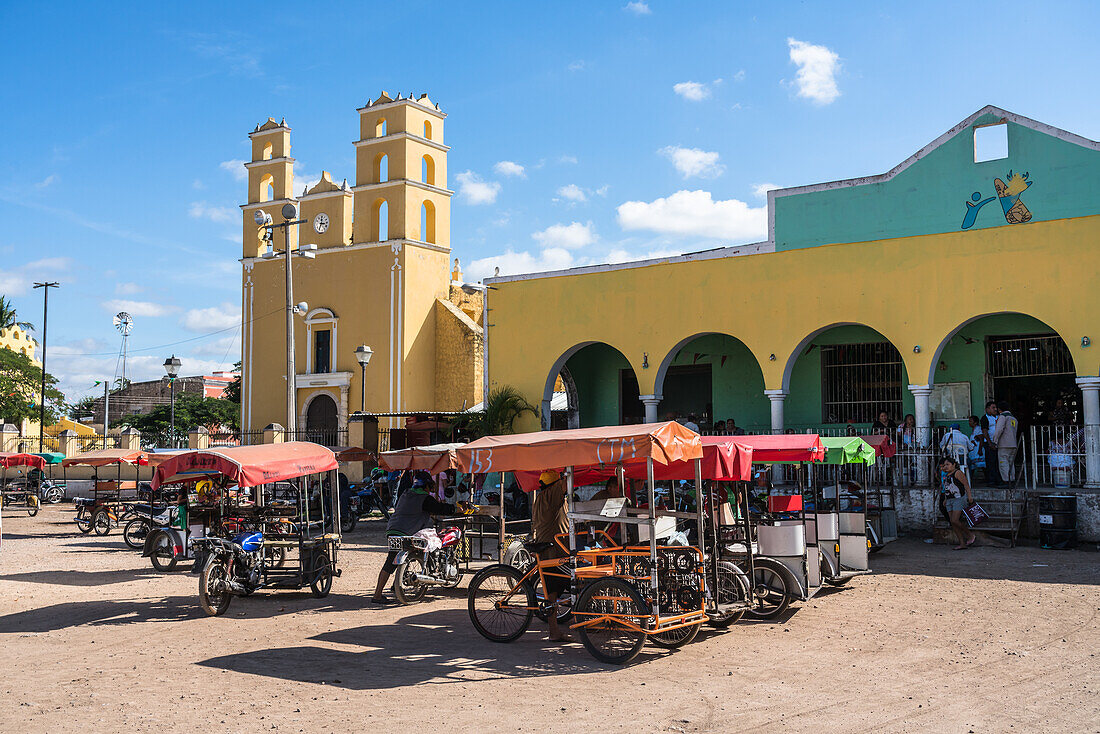 Mototaxis wait for business in front of the 16th Century colonial Church of Nuestra Senora de la Natividad or Our Lady of the Nativity and the market in Acanceh, Yucatan, Mexico.