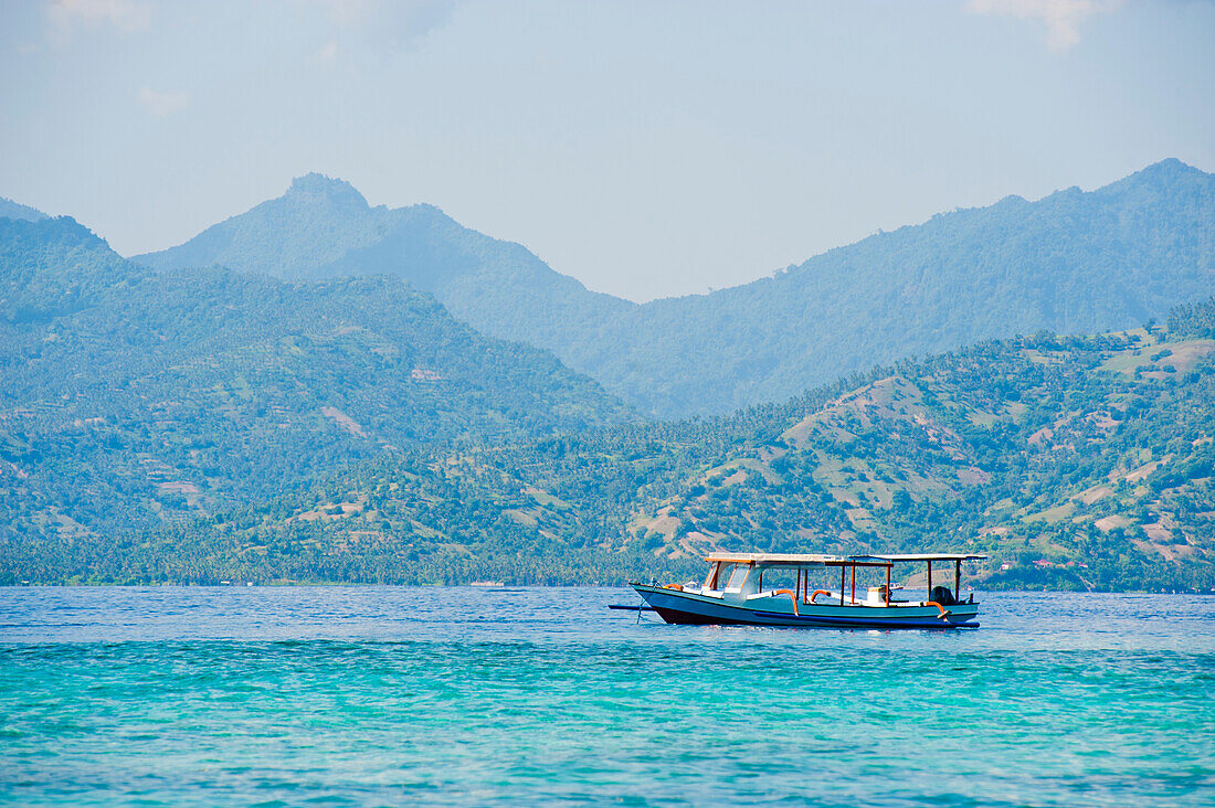 Foto von einem traditionellen indonesischen Boot auf den Gili-Inseln, Indonesien. Im Hintergrund sind die Berge von Lombok zu sehen.