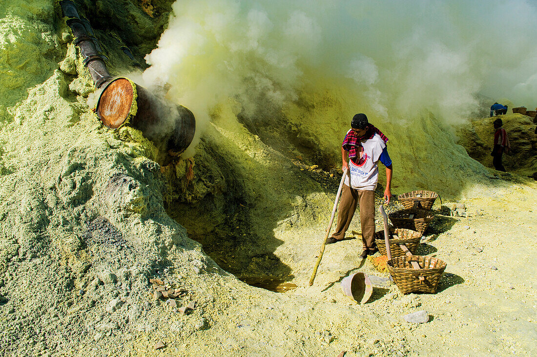 Schwefelbergmann bei der Arbeit am Kawah Ijen, Java, Indonesien. Kawah Ijen ist ein Vulkan mit einem aktiven Krater und einem Säuresee in Ost-Java, Indonesien. Er ist ein unglaubliches und unverzichtbares Ziel für jeden, der Java oder Bali besucht. Nicht nur die Aussicht auf der 4 km langen Wanderung zum Kraterrand ist beeindruckend, sondern auch das, was sich dort abspielt, ist atemberaubend. Auf dem Weg zum Boden des Kwah Ijen (Ijen-Krater) bauen Hunderte von indonesischen Männern, viele in Flipflops, Schwefel aus dem Herzen des Vulkans ab. Sie beladen ihre Körbe mit bis zu 80 kg Schwefel, b