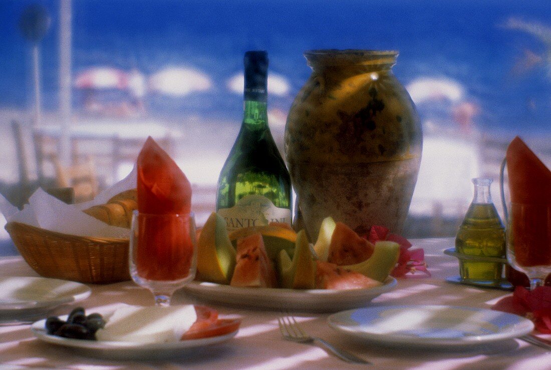 Gedeckter griechischer Tisch mit Wein, Melonen, Brot, Öl etc.