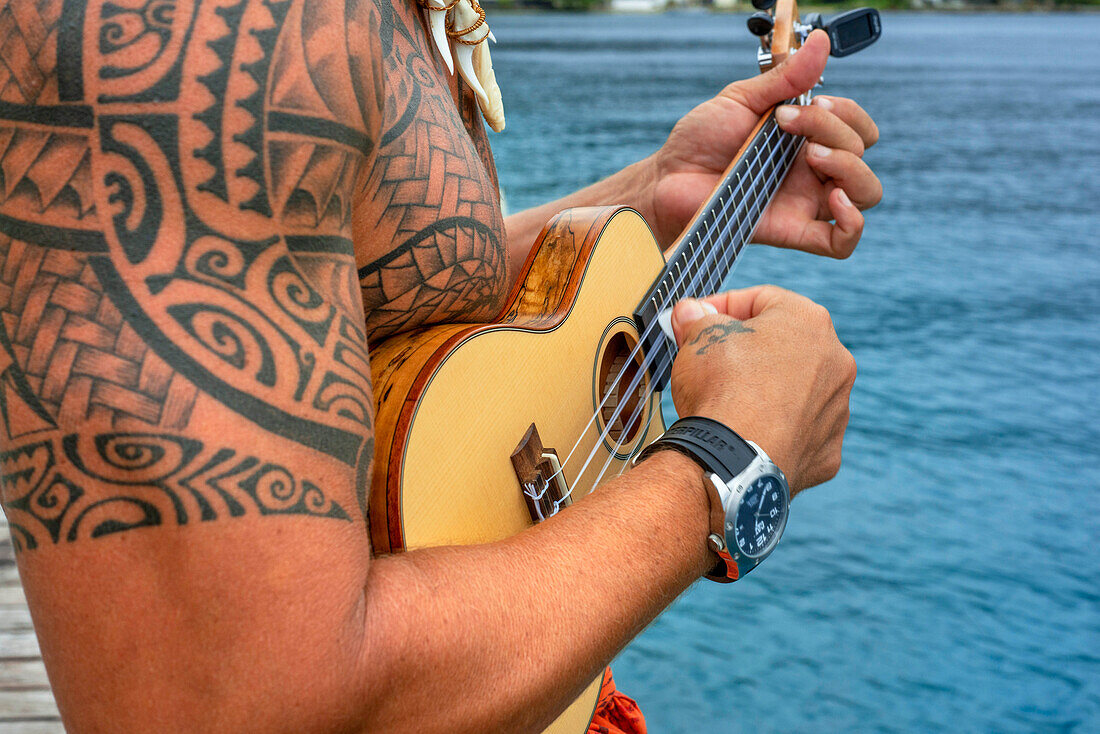 Tätowierter Einheimischer spielt Ukulele in Huahine, Gesellschaftsinseln, Französisch-Polynesien, Südpazifik.