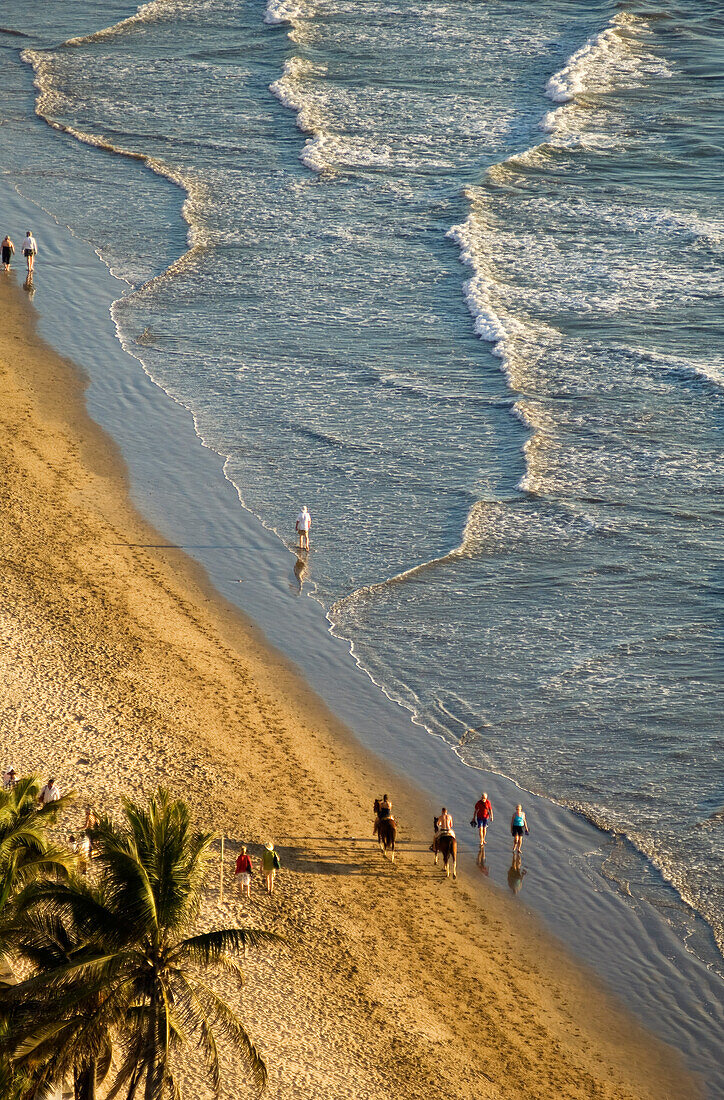 People walking and horseback riding on the beach in the Zona Dorada at El Cid Resort; Mazatlan, Sinaloa, Mexico.