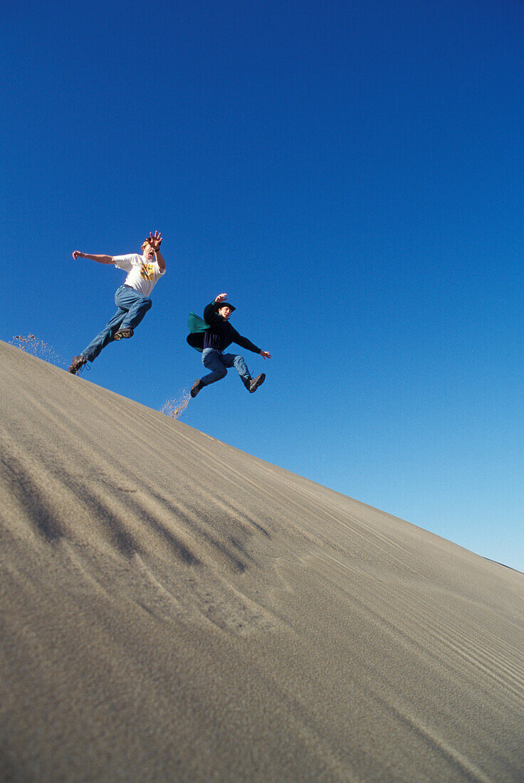Zwei junge Männer springen von einem Dünenkamm; Oregon Dunes National Recreation Area, Umpqua Dunes Abschnitt, Oregon Küste. .