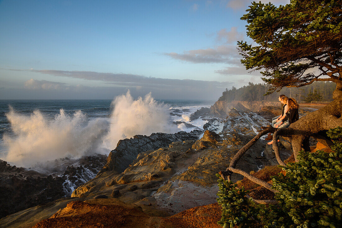 Three women watching storm surf crashing on the rocks at Shore Acres State Park on the southern Oregon coast.