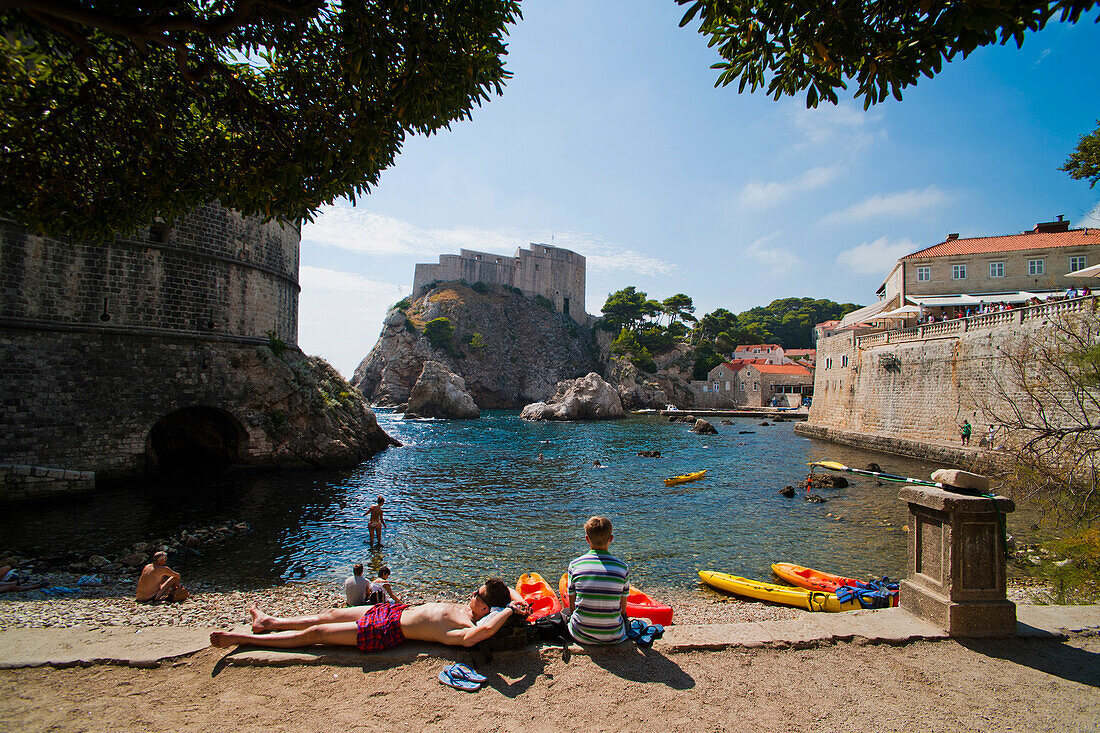 People relaxing on Dubrovnik beach, opposite Fort Lovrijenac, Dubrovnic, Croatia. This is a photo of people relaxing on a small beach in Dubrovnik, opposite Fort Lovrijenac, Croatia. Fort Lovrijenac is a large fort situated on top of a rocky cliff, just outside Dubrovnik Old Town.