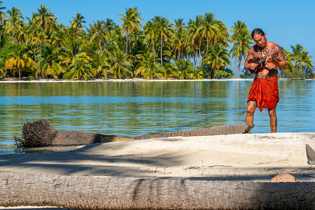 Insel Taha'a, Französisch-Polynesien. Ein einheimischer Junge spielt Ukulele, um ein Mädchen auf dem Motu Mahana zu umwerben, Taha'a, Gesellschaftsinseln, Französisch-Polynesien, Südpazifik.