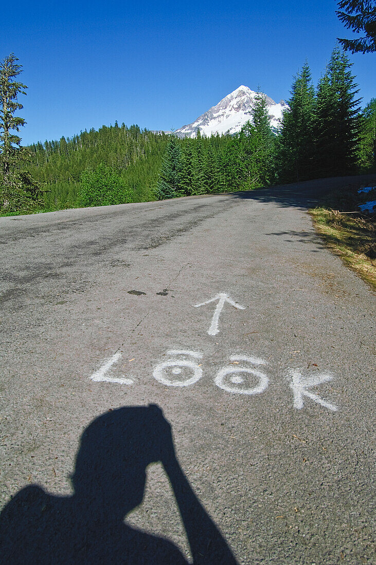 Mount Hood from Lolo Pass with "Look" painted on road and silhouette of photographer.