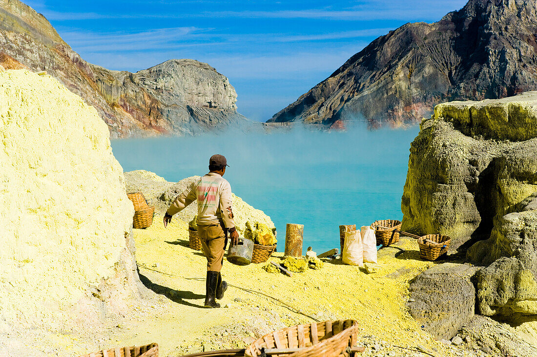 Schwefelarbeiter am Kawah Ijen, Java, Indonesien. Kawah Ijen ist ein Vulkan mit einem aktiven Krater und einem Säuresee in Ost-Java, Indonesien. Er ist ein unglaubliches und unverzichtbares Ziel für jeden, der Java oder Bali besucht. Nicht nur die Aussicht auf der 4 km langen Wanderung zum Kraterrand ist beeindruckend, sondern auch das, was sich dort abspielt, ist atemberaubend. Auf dem Weg hinunter zum Boden des Kwah Ijen (Ijen-Krater) bauen Hunderte von indonesischen Männern, viele in Flipflops, Schwefel aus dem Herzen des Vulkans ab. Sie beladen ihre Körbe mit bis zu 80 kg Schwefel, bevor s