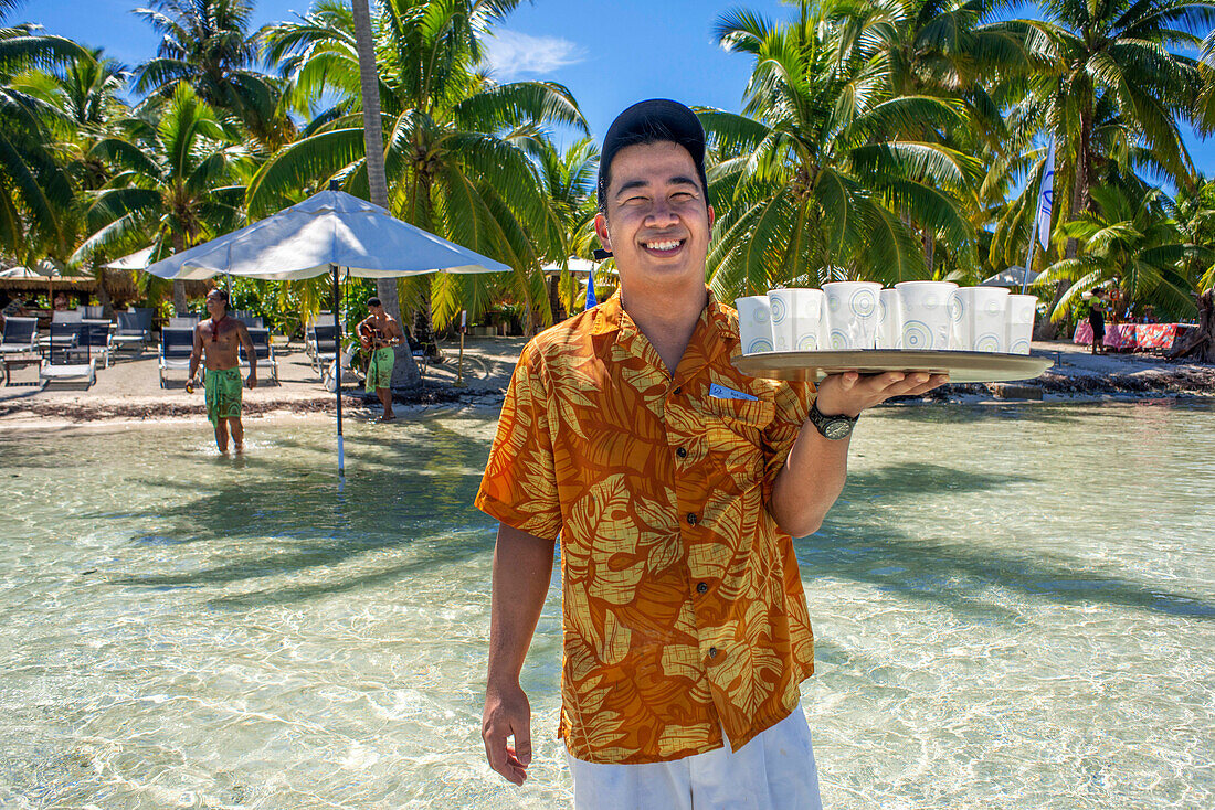 Ein Kellner serviert Cocktails im Inselresort Taha'a, Französisch-Polynesien. Motu Mahana Palmen am Strand, Taha'a, Gesellschaftsinseln, Französisch-Polynesien, Südpazifik.