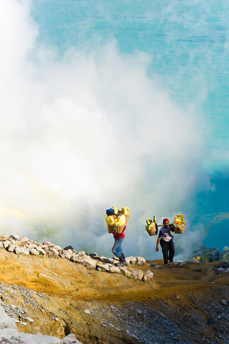 Schwefelarbeiter am Kawah Ijen, Java, Indonesien. Kawah Ijen ist ein Vulkan mit einem aktiven Krater und einem Säuresee in Ost-Java, Indonesien. Er ist ein unglaubliches und unverzichtbares Ziel für jeden, der Java oder Bali besucht. Nicht nur die Aussicht auf der 4 km langen Wanderung zum Kraterrand ist beeindruckend, sondern auch das, was sich dort abspielt, ist atemberaubend. Auf dem Weg zum Boden des Kwah Ijen (Ijen-Krater) bauen Hunderte von indonesischen Männern, viele in Flipflops, Schwefel aus dem Herzen des Vulkans ab. Sie beladen ihre Körbe mit bis zu 80 kg Schwefel, bevor sie sich a