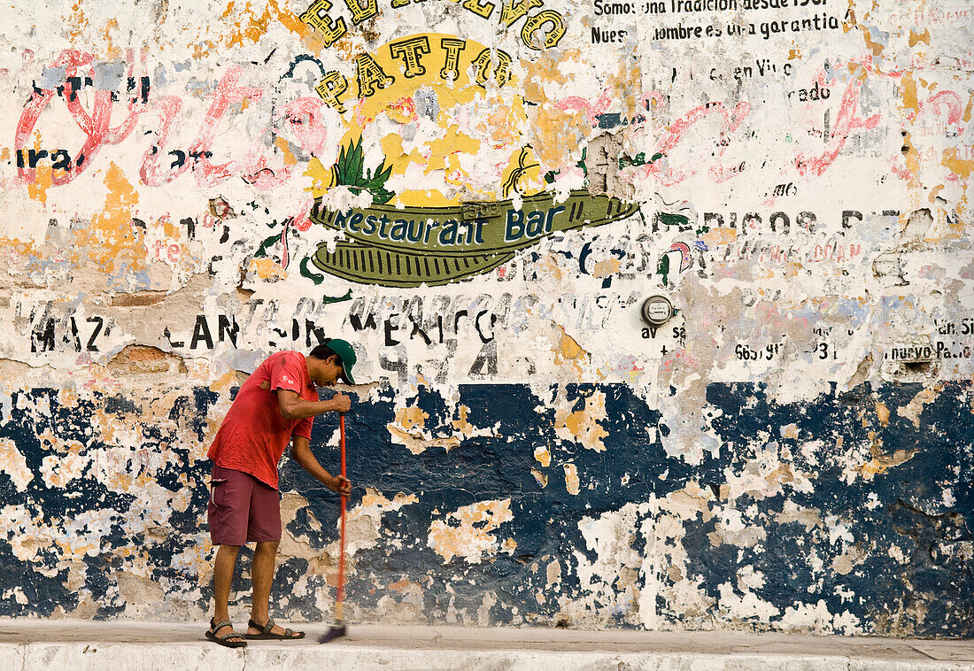 Man sweeping sidewalk and faded signs on wall, Avenida Zaragoza, old town Mazatlan, Mexico.