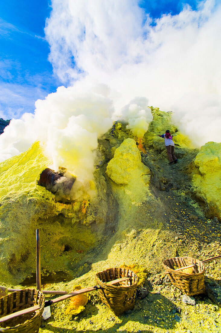 Schwefelbergmann bei der Arbeit am Kawah Ijen, Java, Indonesien. Kawah Ijen ist ein Vulkan mit einem aktiven Krater und einem Säuresee in Ost-Java, Indonesien. Er ist ein unglaubliches und unverzichtbares Ziel für jeden, der Java oder Bali besucht. Nicht nur die Aussicht auf der 4 km langen Wanderung zum Kraterrand ist beeindruckend, sondern auch das, was sich dort abspielt, ist atemberaubend. Auf dem Weg zum Boden des Kwah Ijen (Ijen-Krater) bauen Hunderte von indonesischen Männern, viele in Flipflops, Schwefel aus dem Herzen des Vulkans ab. Sie beladen ihre Körbe mit bis zu 80 kg Schwefel, b