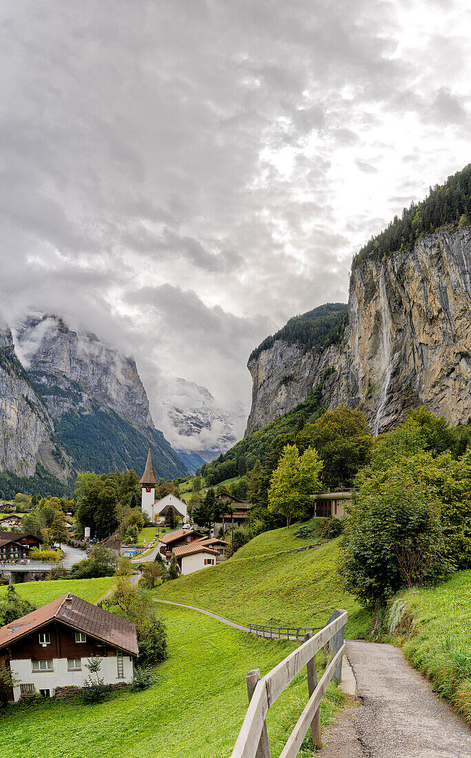 Path among green meadows of the alpine village of Lauterbrunnen with Trummelbach Falls in the background, Bern canton, Switzerland, Europe