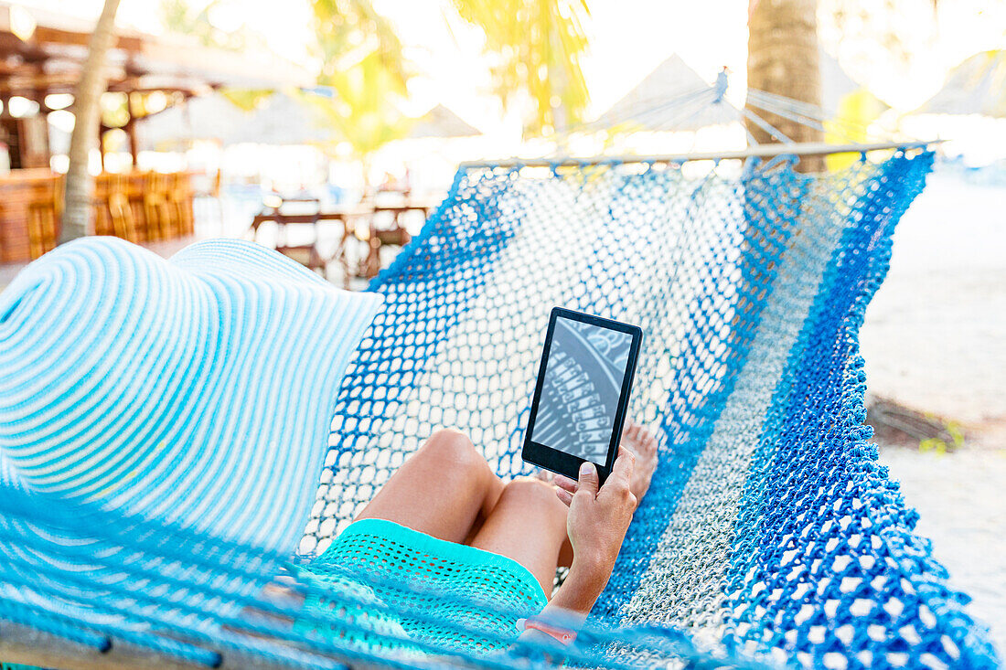 Woman reading from Kindle tablet lying on hammock, Zanzibar, Tanzania, East Africa, Africa