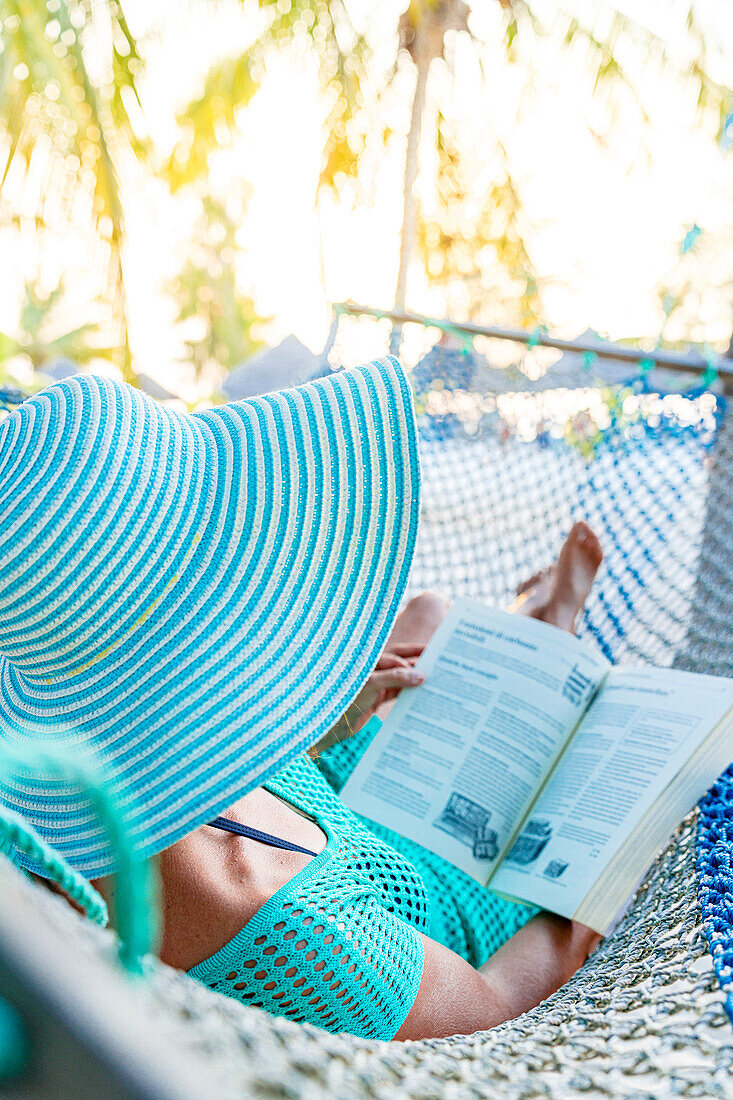 Woman with hat relaxing reading a book in a hammock, Zanzibar, Tanzania, East Africa, Africa