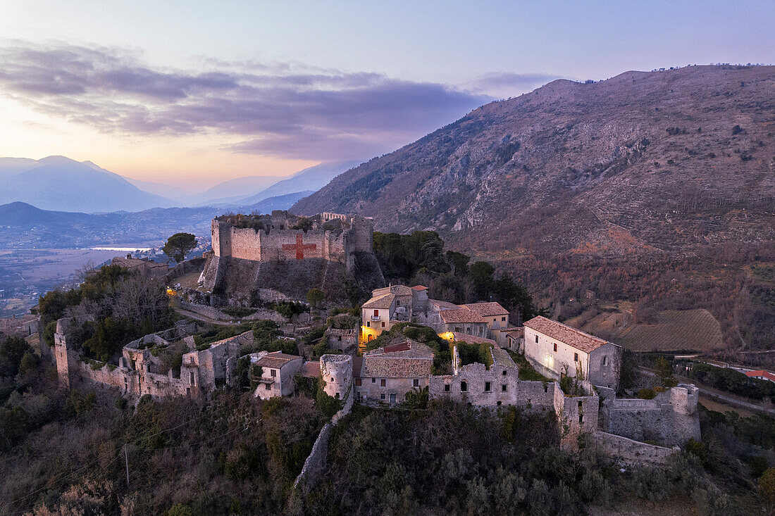 Luftaufnahme der mittelalterlichen Burg von Vicalvi, mit rotem Kreuz auf der Umfassungsmauer, mit Blick auf das beleuchtete alte Dorf in der Abenddämmerung, Vicalvi, Provinz Frosinone, Ciociaria, Region Latium, Latium, Italien, Europa