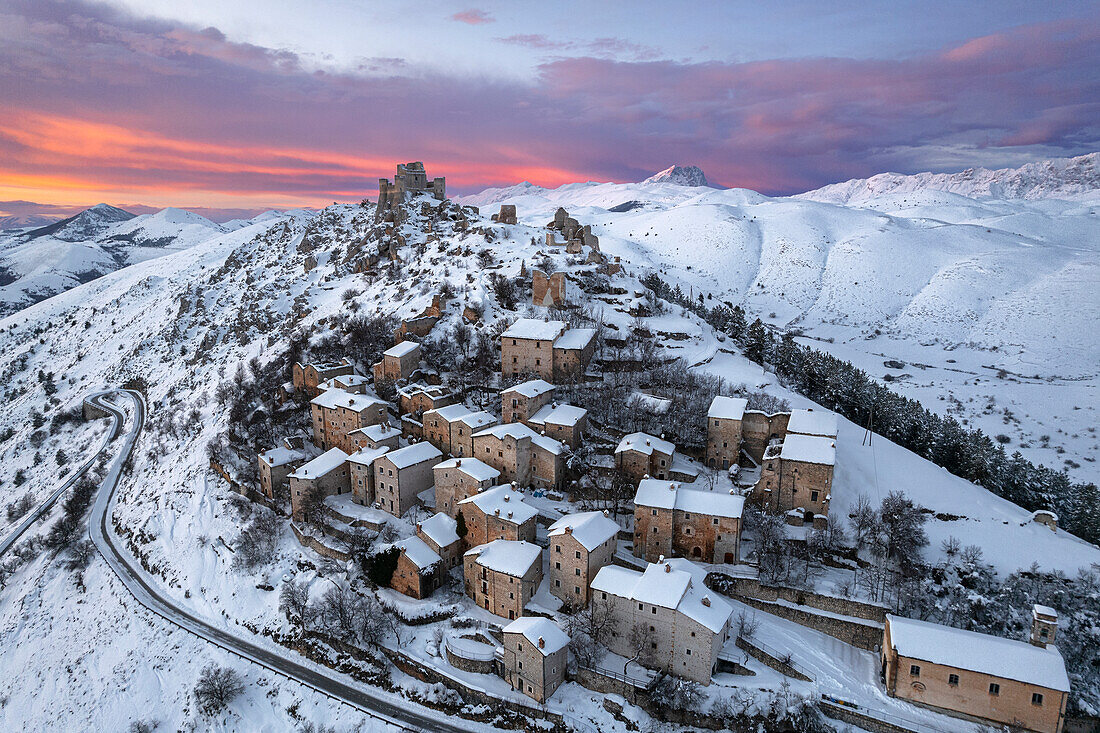 Aerial winter view of the snow covered medieval village of Rocca Calascio with the castle and pink clouds at dusk, Rocca Calascio, Gran Sasso e Monti della Laga National Park, Campo Imperatore, L'Aquila province, Abruzzo region, Italy, Europe