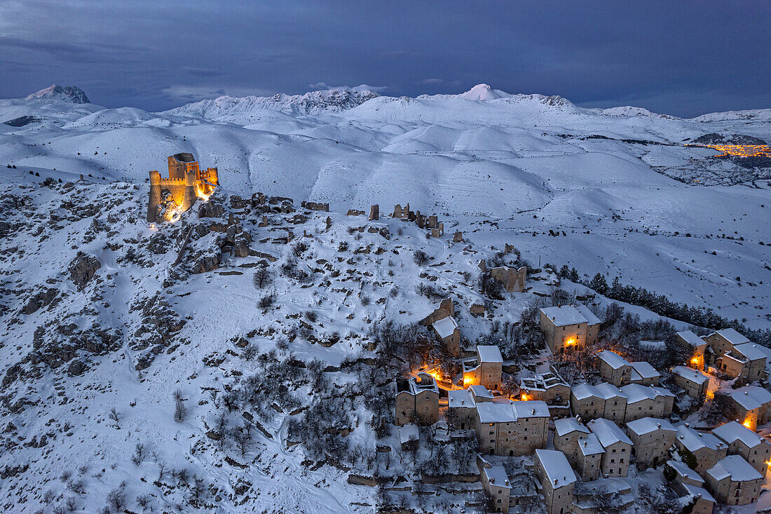 Winteransicht des schneebedeckten, beleuchteten mittelalterlichen Dorfes Rocca Calascio mit der Burg in der Abenddämmerung, Rocca Calascio, Nationalpark Gran Sasso e Monti della Laga, Campo Imperatore, Provinz L'Aquila, Region Abruzzen, Italien, Europa