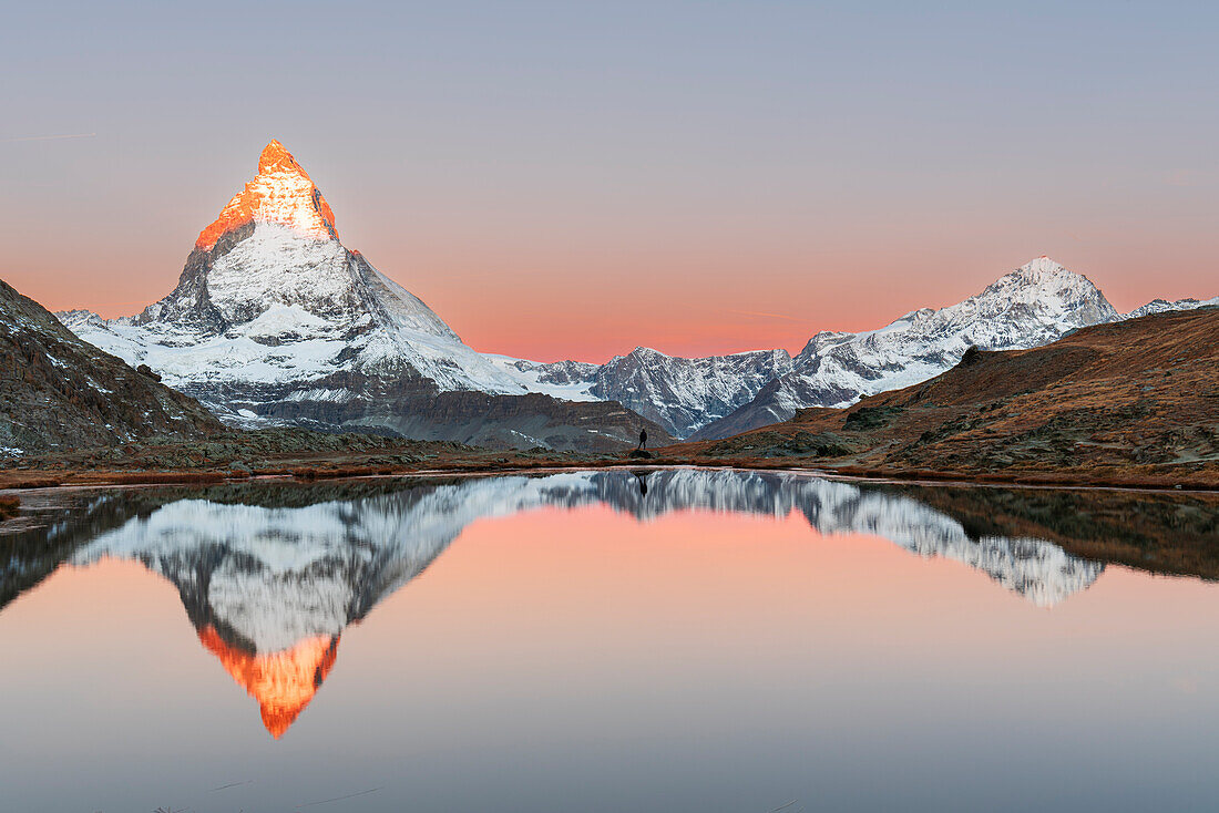 Hiker admiring the Matterhorn reflected in the Riffelsee lake at sunrise, Gornergrat, Zermatt, canton of Valais, Switzerland, Europe