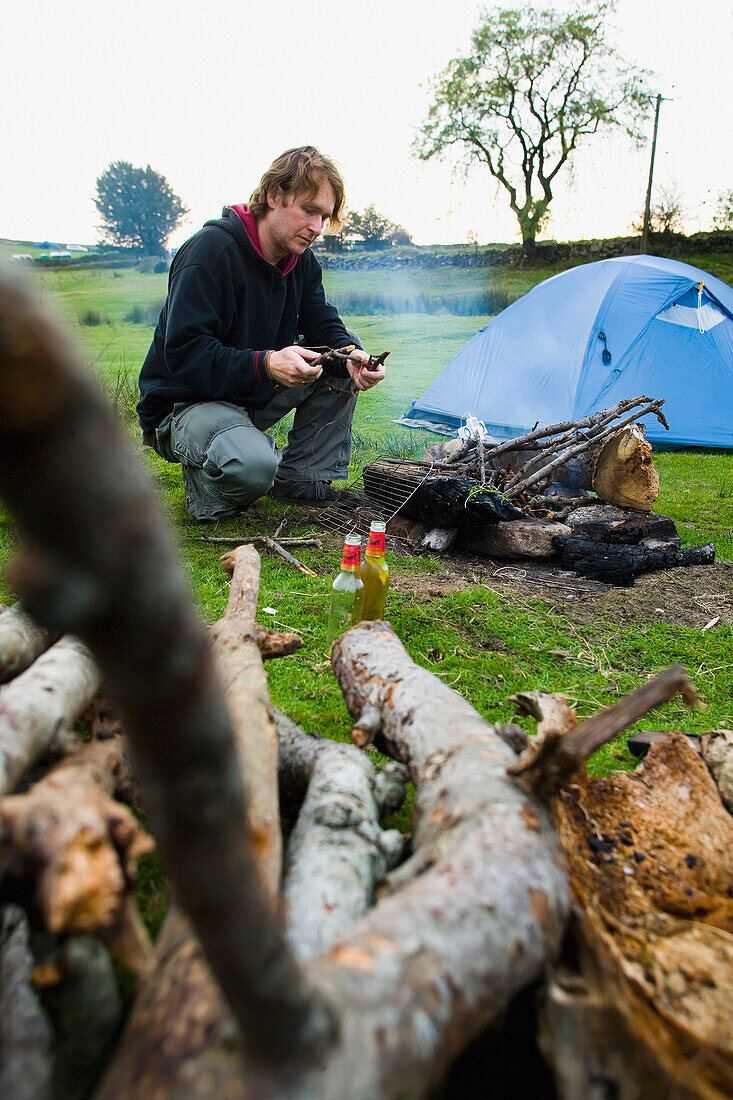 Male Preparing A Open Log Fire While Camping